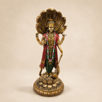 Standing Vishnu idol beneath a Sheshnag serpent canopy, with a gold-tone finish, red drape, green clothing and floral garland, front view