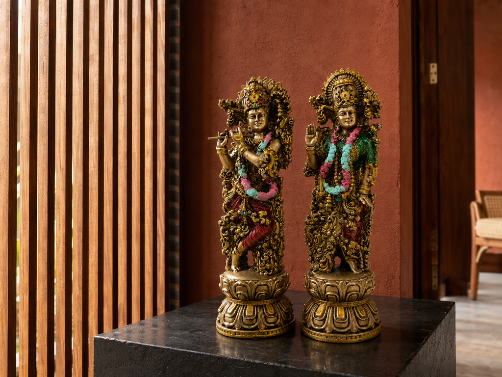 Antique gold-tone Radha–Krishna idol pair styled on a dark tabletop in a veranda
