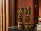 Antique gold-tone Radha–Krishna idol pair styled on a dark tabletop in a veranda