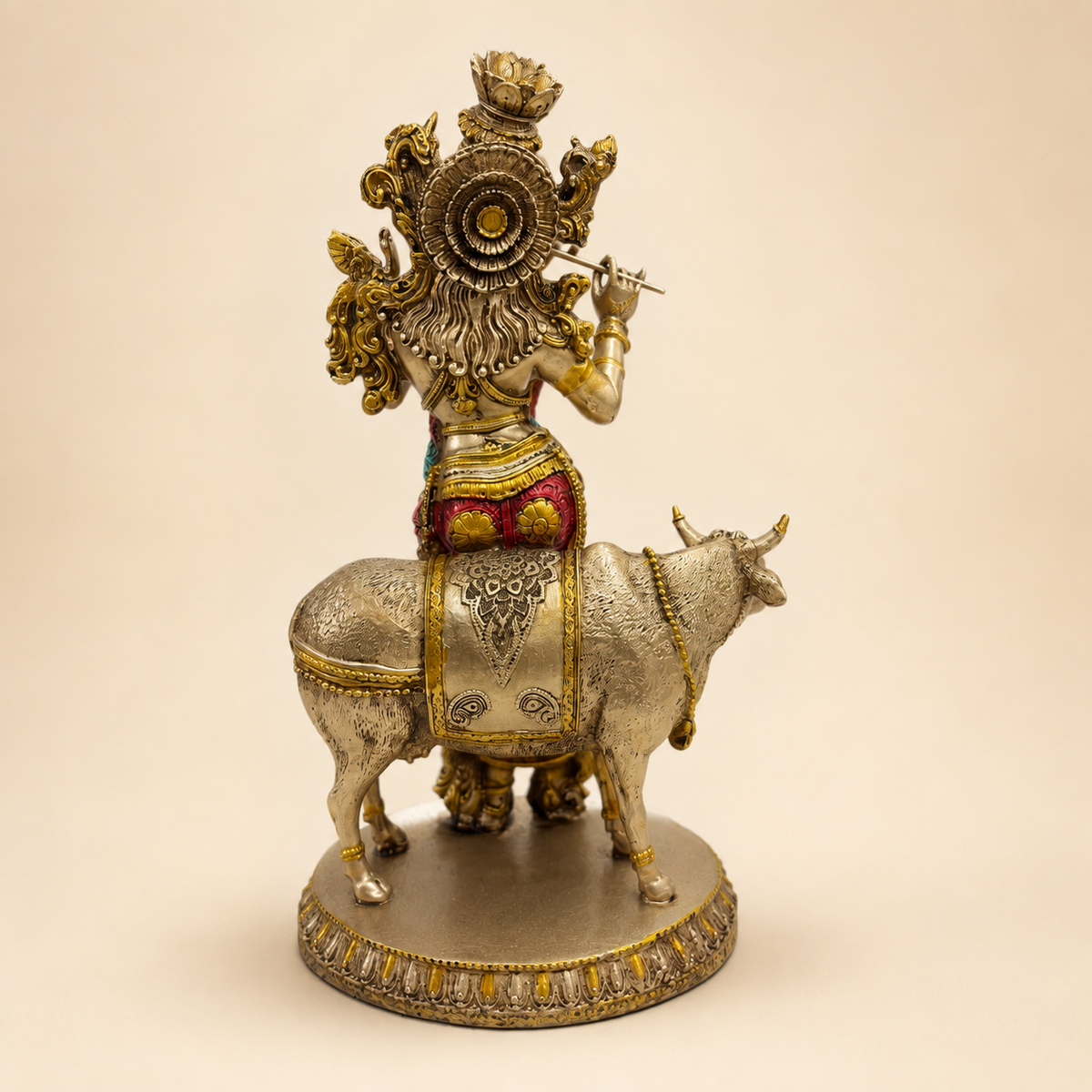 Rear view of the Krishna and cow idol showing the decorated headdress, flowing hair, patterned cow adornment and round base