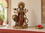 Durga idol and lion displayed on a sunlit altar beside a bowl with a red flower