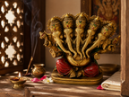 Five-faced Ganesha idol in a warm prayer setting with a diya, incense, flowers and folded fabric