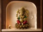 Ganesha idol with a bowl of sweets displayed in an arched prayer niche beside a diya