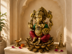 Ganesha idol on a lotus base displayed in a warm shrine with a diya, bell, incense and flower petals