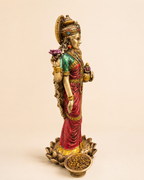 Angled view of the Lakshmi idol showing red and green attire, crown and lotus-style base