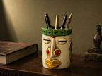 Nomad Bloom decorative face pen stand holding pens on a dark wood desk