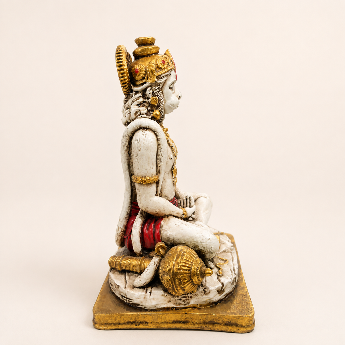 Side view of the seated Hanuman idol showing the crown, curled tail and gold-tone gada