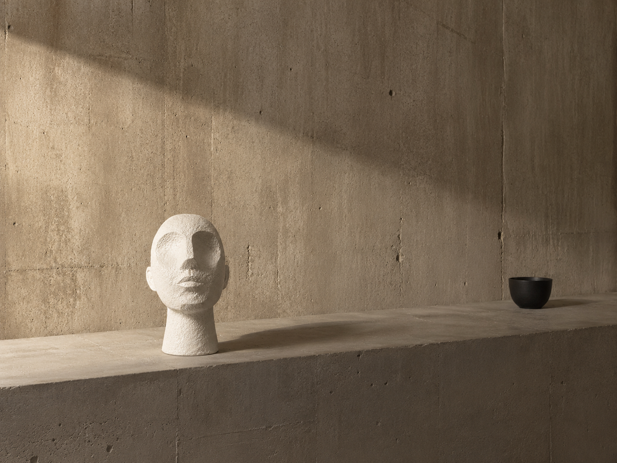 Textured white abstract face sculpture styled on a minimalist concrete ledge