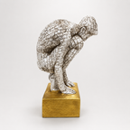 Silver-toned crouching mosaic figure sculpture on a gold base, side view