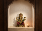 Ganesha idol displayed in a simple arched prayer niche beside a glowing diya