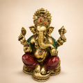 Seated Ganesha idol with ornate crown, gold-tone finish, red dhoti and green shawl, front view