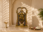 Tirupati Balaji idol displayed on a light stone home mandir counter with lamps and flowers